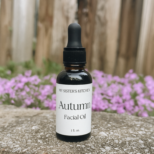 Bottle of 'Autumn Facial Oil' from 'My Sister's Kitchen' on a stone surface with pink flowers in the background.